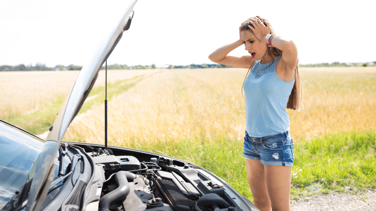 A woman holding her head looking at a broken car.