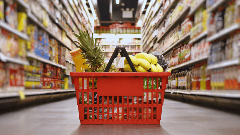 A grocery basket full of groceries on the floor of a grocery store.