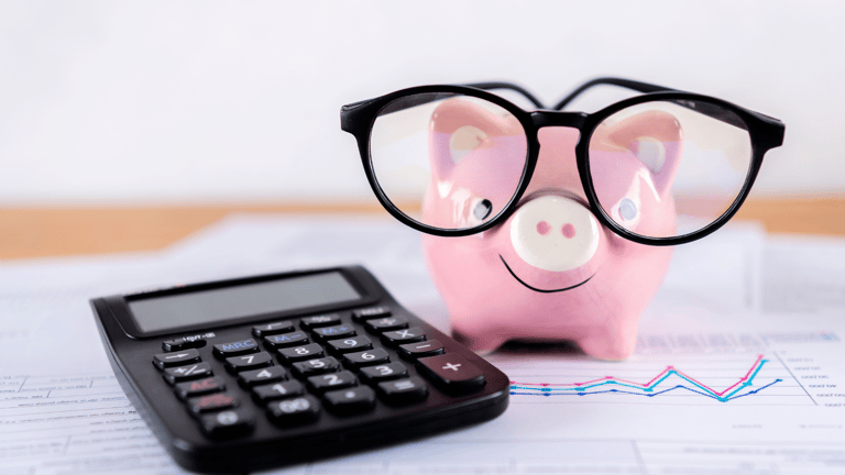 A piggy bank wearing glasses next to a calculator.